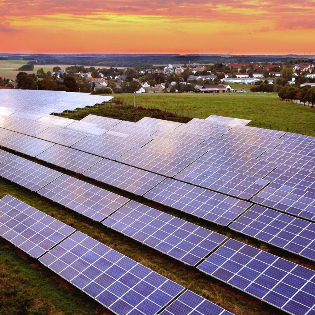 Solarpark von Wattner bei Sonnenuntergang auf grüner Freifläche nahe einer Ortschaft – nachhaltige Energiegewinnung durch Photovoltaik in ländlicher Umgebung.